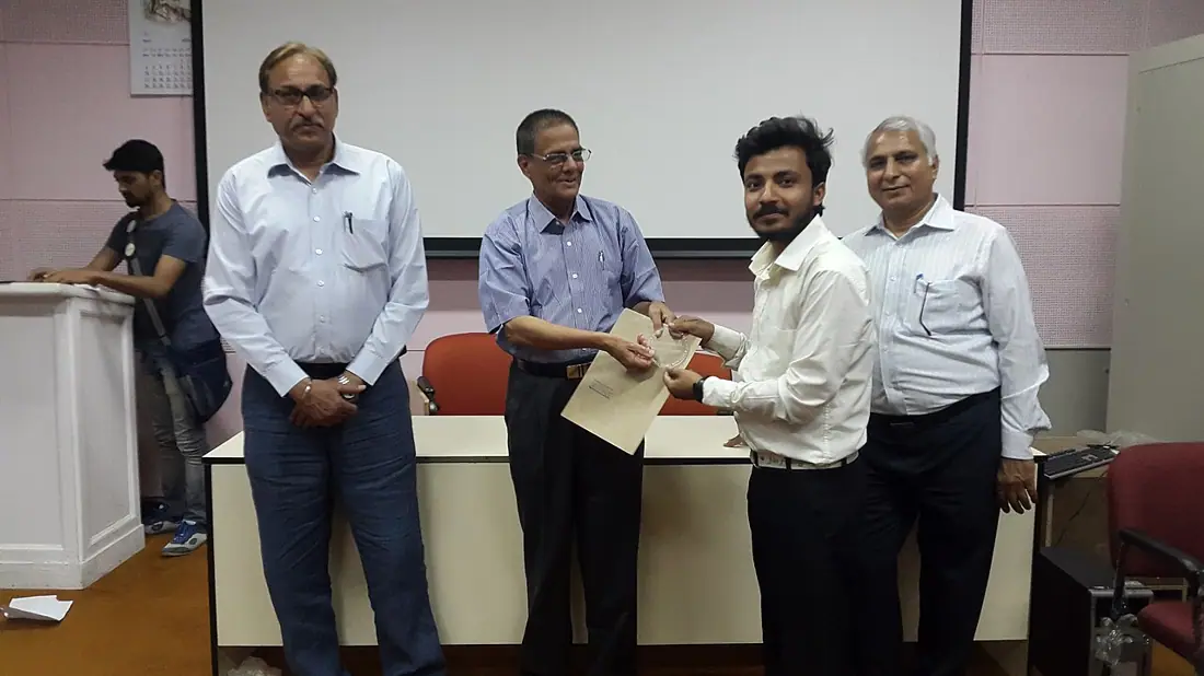 Five men at an event at IGNOU, one receiving a document.