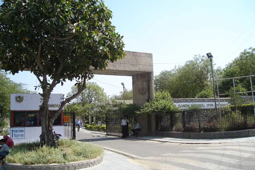 Main entrance gate of IGNOU, with its name, trees, and people.